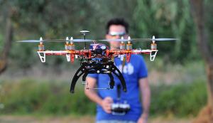 Un drone per uso civile a più eliche e sulla sfondo il pilota con il radiocomando